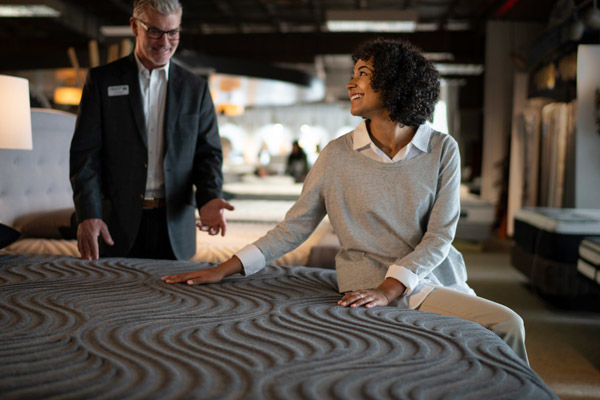 Woman shopping for a mattress sitting on bed with a salesperson